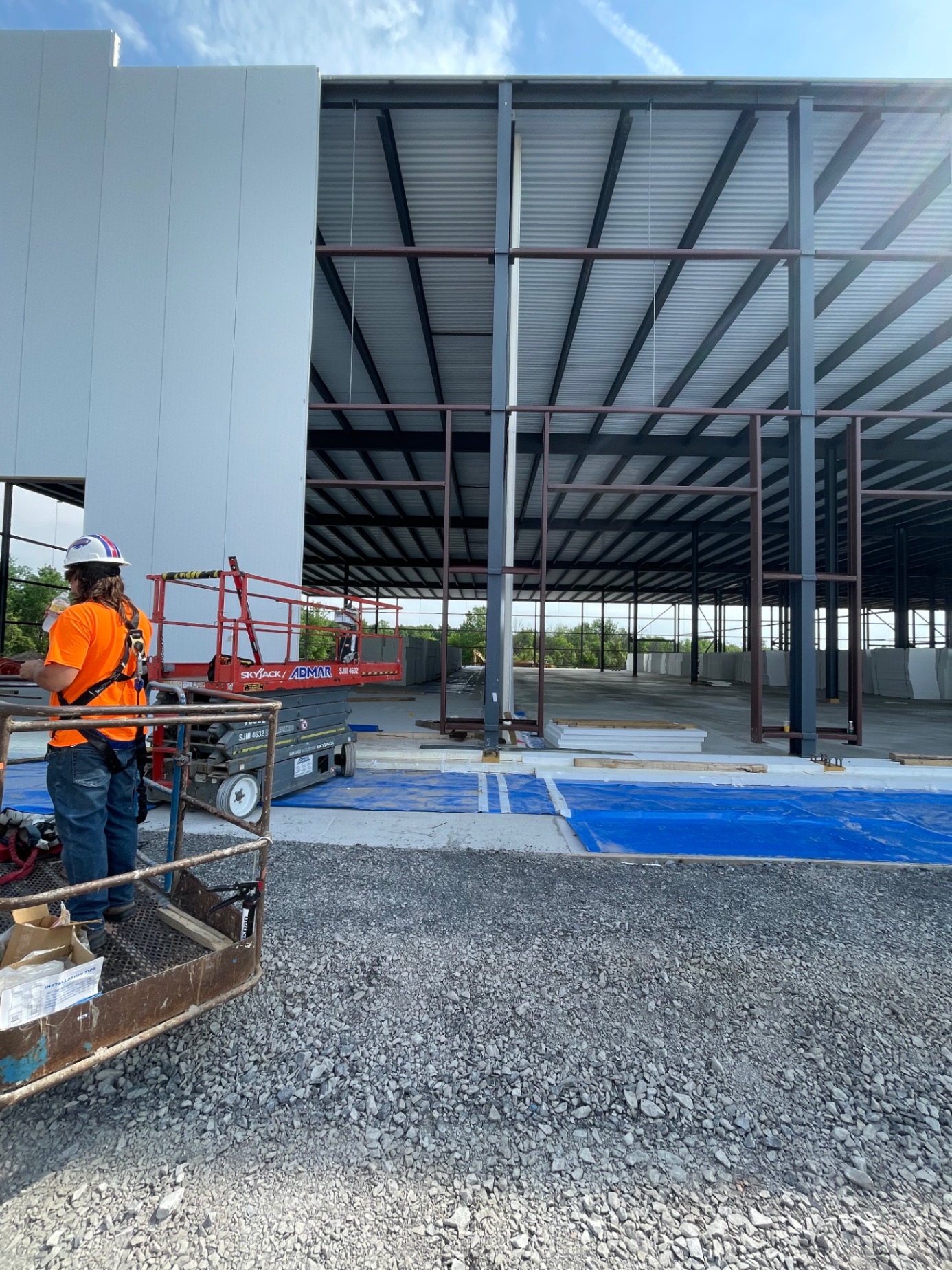 Worker on site — large steel structure with scissor lift